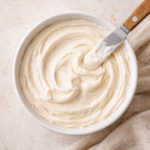 Bowl of smooth vegan cream cheese frosting with soft swirls, showing a thick, creamy texture ready for spreading on cakes and cupcakes.